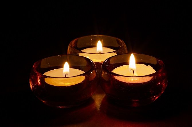 Group of three burning tea-lights in coloured glass candle-holders, dark black background